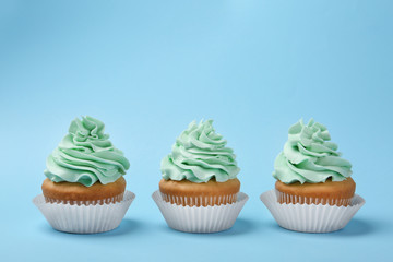 Tasty cupcakes with cream on light blue background