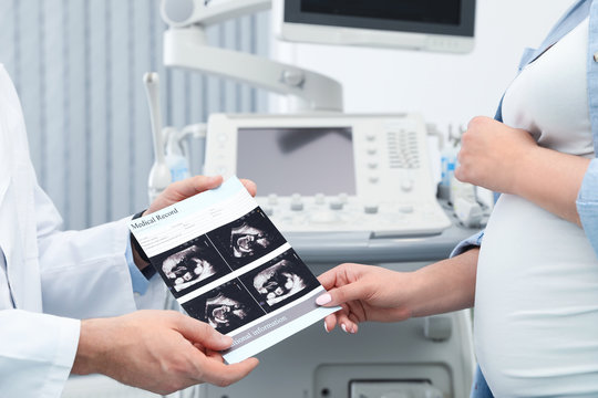 Doctor showing ultrasound images of baby to future mother in clinic, closeup
