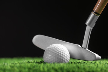 Hitting golf ball with club on artificial grass against black background, space for text