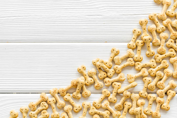 Dry puppy food in shape of bone on white wooden background top view copyspace