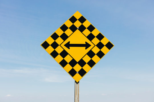 View of arrow intersection sign against cloudy sky