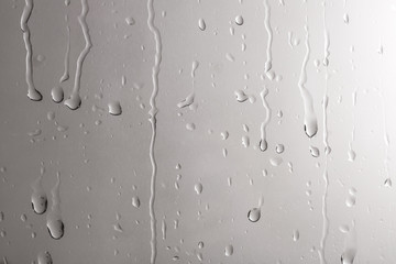 Glass with rain drops against light background