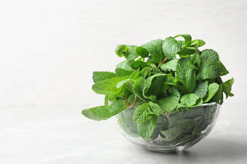 Glass bowl full of fresh green mint on light background, space for text