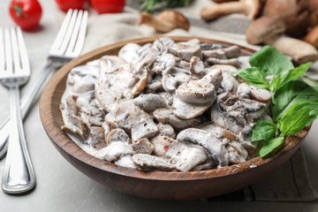 Wooden bowl with delicious cooked mushrooms on table, closeup
