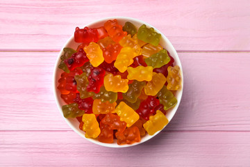 Bowl with delicious bright jelly bears on pink wooden table, top view