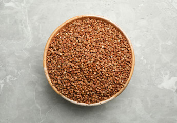 Bowl of uncooked buckwheat on grey marble table, top view