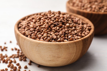 Wooden bowl full of uncooked buckwheat on white table, closeup