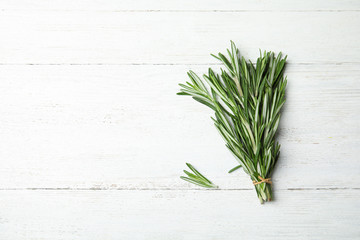 Bunch of fresh rosemary on white wooden table, top view with space for text