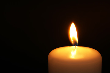 Burning candle on dark background, closeup with space for text. Symbol of sorrow