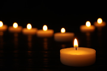 Burning candle on black table against blurred background, space for text