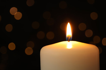 Burning candle on black background with blurred lights, space for text