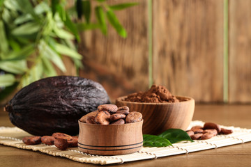 Bowl of cocoa beans, pod and powder on table, space for text