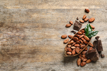 Flat lay composition with cocoa beans and chocolate pieces on wooden table, space for text