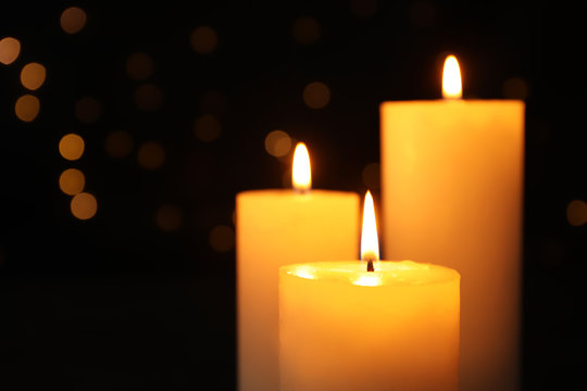Burning candles on black background with blurred lights, space for text