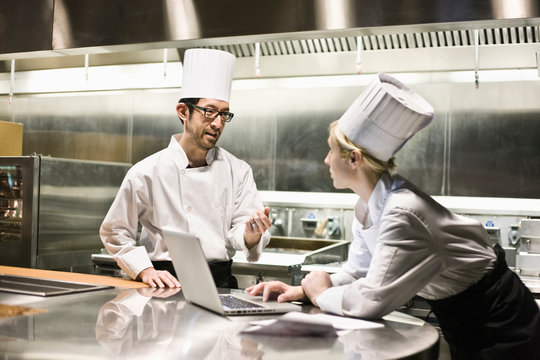 Chefs talking while working on laptop in commercial kitchen