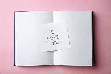Piece of paper with phrase I LOVE YOU and notebook on pink background, top view