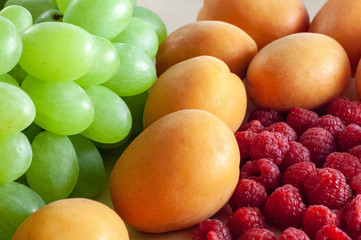Fresh green grape, raspberry and ripe apricots on top of wooden textural surface. Close-up