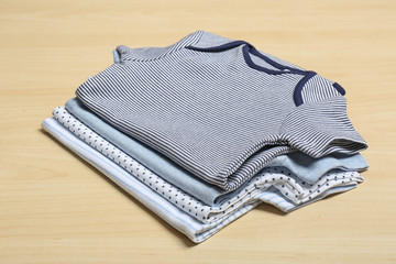 Different cute baby bodysuits on wooden background