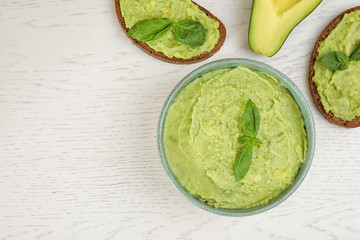 Flat lay composition with guacamole, sandwiches and avocado on white wooden table. Space for text