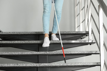 Blind person with long cane going down stairs indoors, closeup