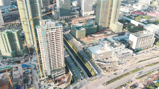 Drone rises smoothly. We see a large under construction a new neighborhood. In the frame of building frames, construction cranes. In streets drive cars. Guangzhou, China