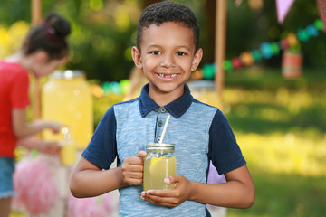 Cute little African-American boy with natural lemonade in park. Summer refreshing drink