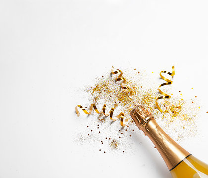 Bottle of champagne with gold glitter, confetti and space for text on white background, top view. Hilarious celebration