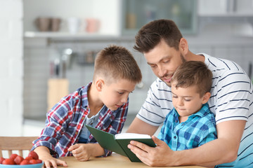 Dad and his sons reading interesting book in kitchen