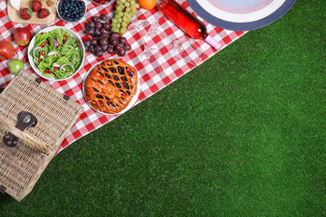 Flat lay composition with picnic basket and products on checkered blanket, space for text