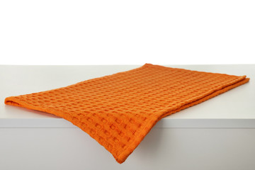 Folded orange kitchen towel on light table against white background
