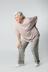 Full length portrait of senior woman having knee problems on grey background