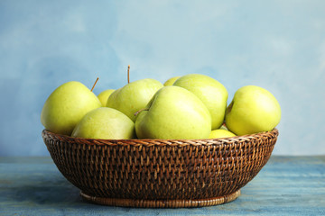 Wicker bowl of fresh ripe green apples on wooden table against blue background