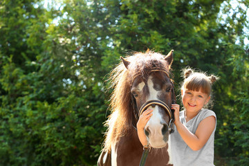 Cute little girl with her pony in green park