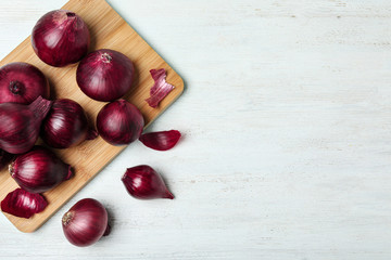 Board and red onions on white wooden table, flat lay. Space for text