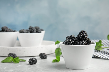 Fototapeta na wymiar Bowls of tasty blackberries on grey marble table. Space for text