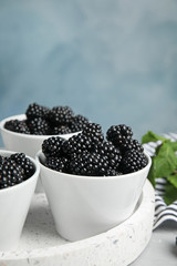Tray with bowls of tasty blackberries on grey marble table against blue background