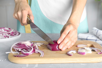 Obraz na płótnie Canvas Woman cutting fresh red onion on wooden board at table, closeup