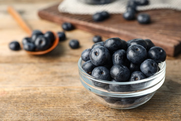 Bowl of fresh acai berries on wooden table, closeup. Space for text