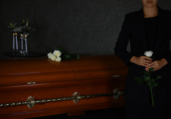Young woman with white rose near casket in funeral home, closeup