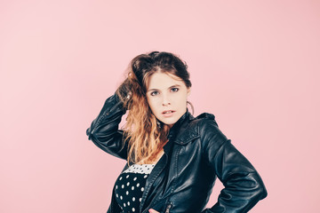 Beautiful glamour girl  wearing leather jacket and black dress with white polka dots posing on pink background. Fashion concept. Portrait of stylish European young woman.