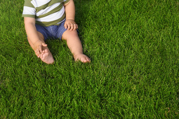 Adorable little baby sitting on green grass outdoors, closeup