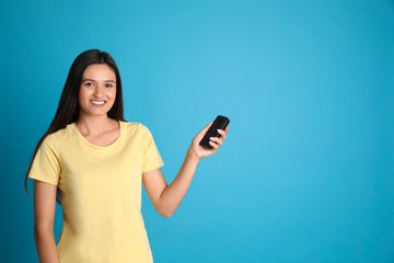 Fototapeta premium Happy young woman operating air conditioner with remote control on light blue background. Space for text