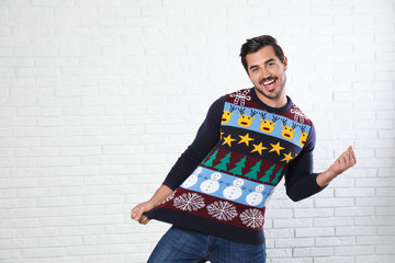 Portrait of happy man in Christmas sweater near white brick wall