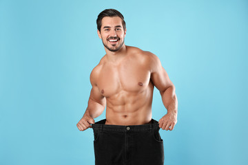 Fototapeta premium Young man with slim body in old big size jeans on light blue background
