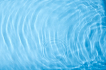 Concentric waves on blue water surface after falling drops, top view