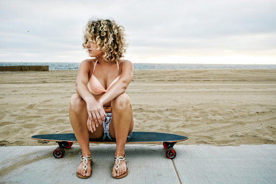 Young woman sitting on skateboard on beach