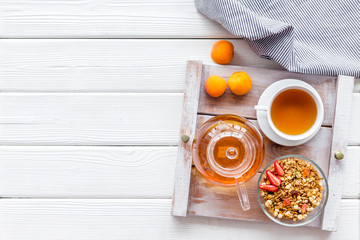 granola, tea and fruit for homemade breakfast on the tray on white wooden background top view copyspace