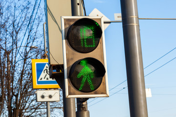 Green traffic light signal for pedestrians at a pedestrian crossing and a digital time display...