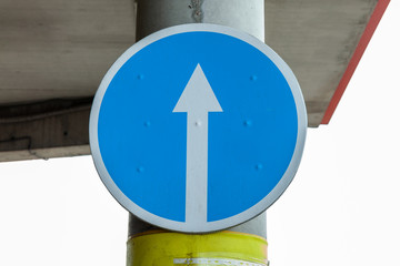 White arrow on blue background of round traffic sign. An entry-inhibiting sign is attached to a...
