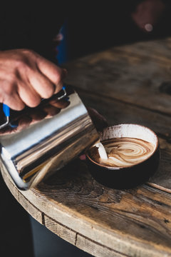 Close up of barista pouring milk from jug into mug